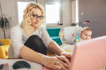 Donna al tavolo con un bambino mentre controlla documenti e spese familiari al computer