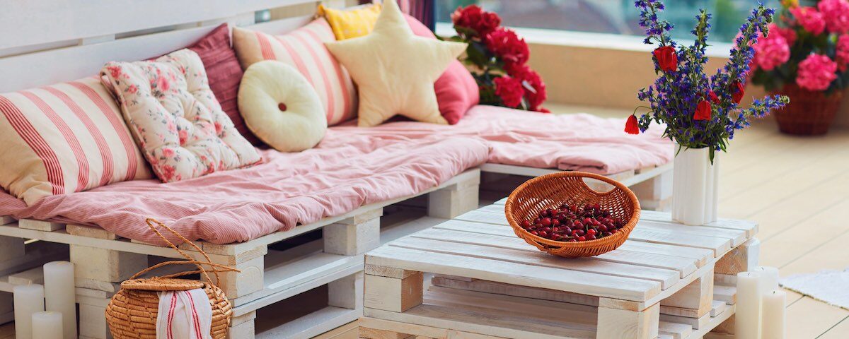 Giardino arredato con divanetto in pallet, tavolino di legno e cassette trasformate in fioriere
