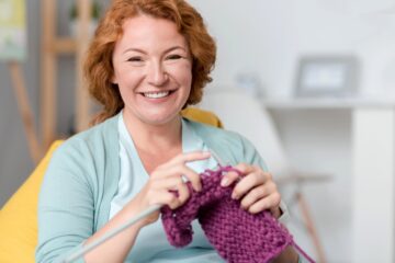 Donna seduta in poltrona mentre usa due ferri per lavorare a maglia un piccolo progetto color crema